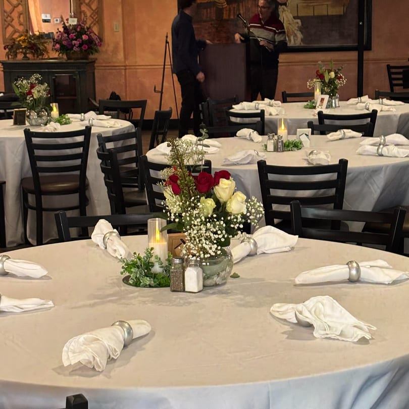 Round tables with white tablecloths, floral centerpieces, and candles, set for an event at Galindo's.