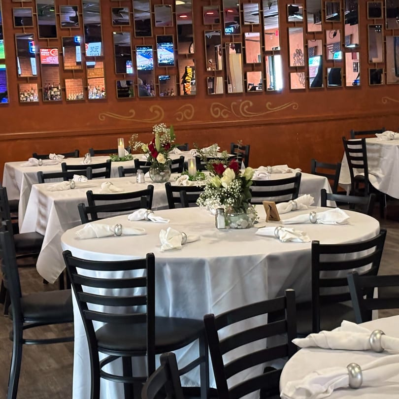 Dining room at Galindo's with white-clothed tables, black chairs, and floral centerpieces under mirrored walls.